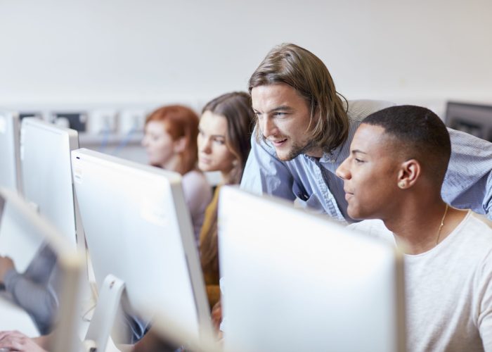 Male lecturer showing student using computer in higher education college computer room